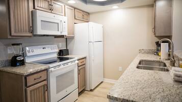A kitchen with a stove, microwave, refrigerator, granite countertop, and wooden cabinets.