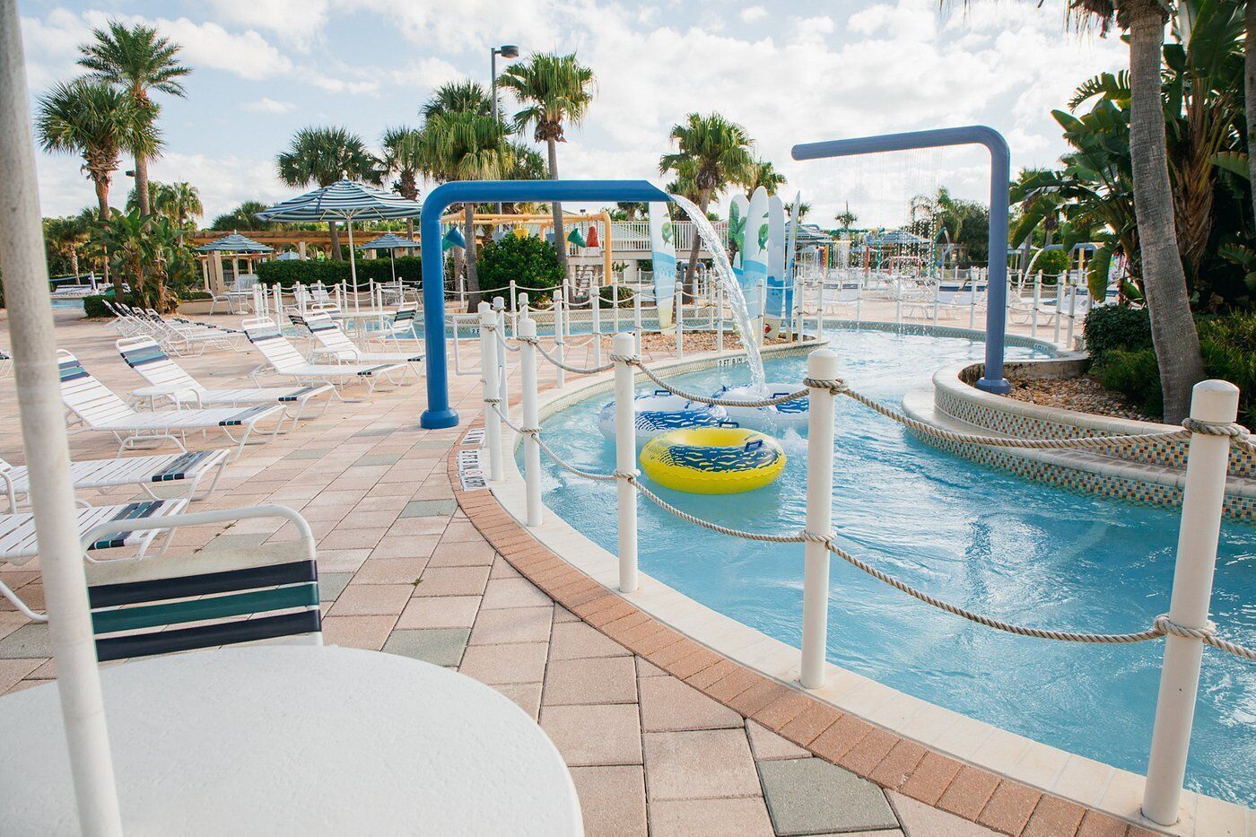 A pool area with lounge chairs, a water slide, and a small inflatable raft.