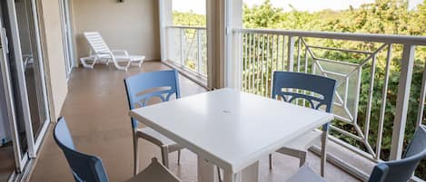 A balcony with a white table and blue chairs, overlooking a garden.