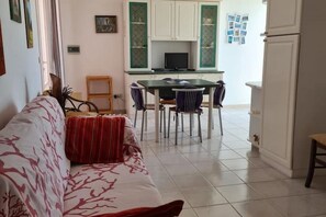 En stue med sofa, spisebord med stole og et køkkenområde med skabe og et køleskab.