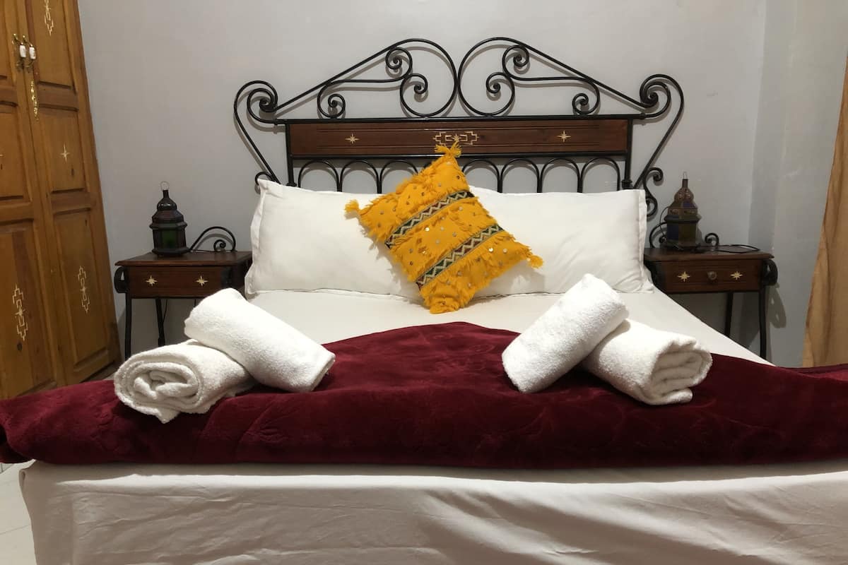 Un lit bien fait, avec des draps blancs, une couverture rouge et deux serviettes enroulées.