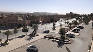 A cityscape with a wide road, palm trees, and traditional buildings. - Aigle Appart Hôtel  (Ouarzazate)