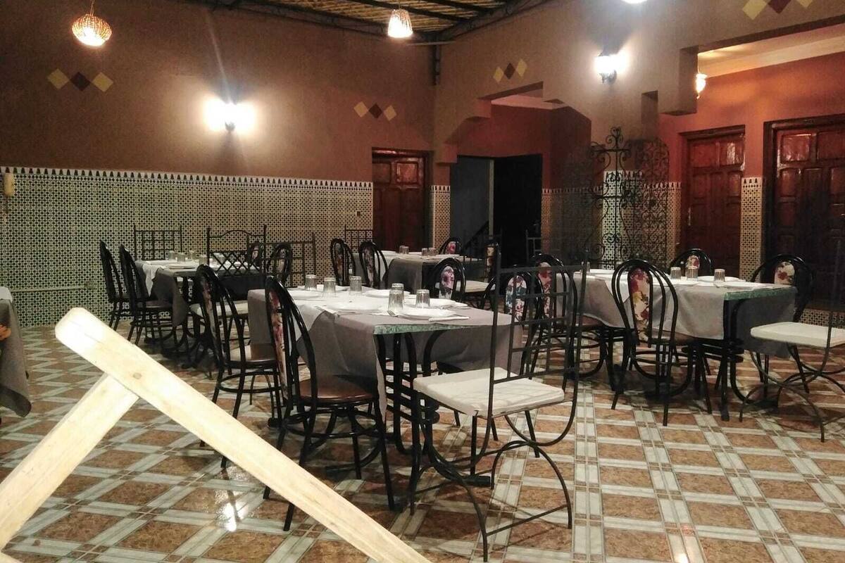 Un restaurant doté de nombreuses tables et chaises, d’un sol carrelé et d’un plafond haut avec des poutres apparentes.