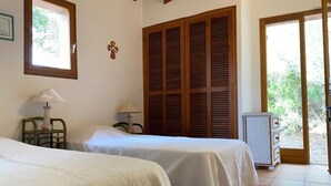 Une chambre avec deux lits, des volets en bois, un radiateur et une vue sur la verdure.
