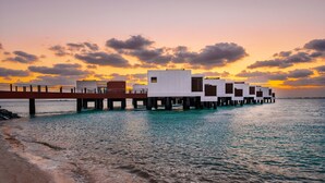 Un hotel frente al agua con bungalows sobre el agua, unidos por un puente.