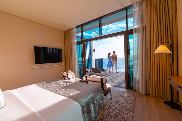 A hotel room with a bed, a TV, a desk, and a view of the sea. - Bab Al Nojoum Hudayriyat Villas (Abu Dhabi)
