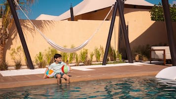 A pool area with a hammock, palm trees, and a building with a beige facade.