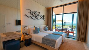 Habitación de hotel con dos camas, un escritorio, una silla, un televisor y un amplio ventanal con vista al océano.