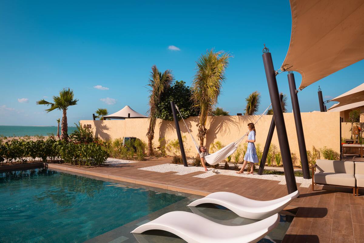Un espace aménagé au bord de la piscine, avec des chaises longues, un palmier et une vue sur l’océan.