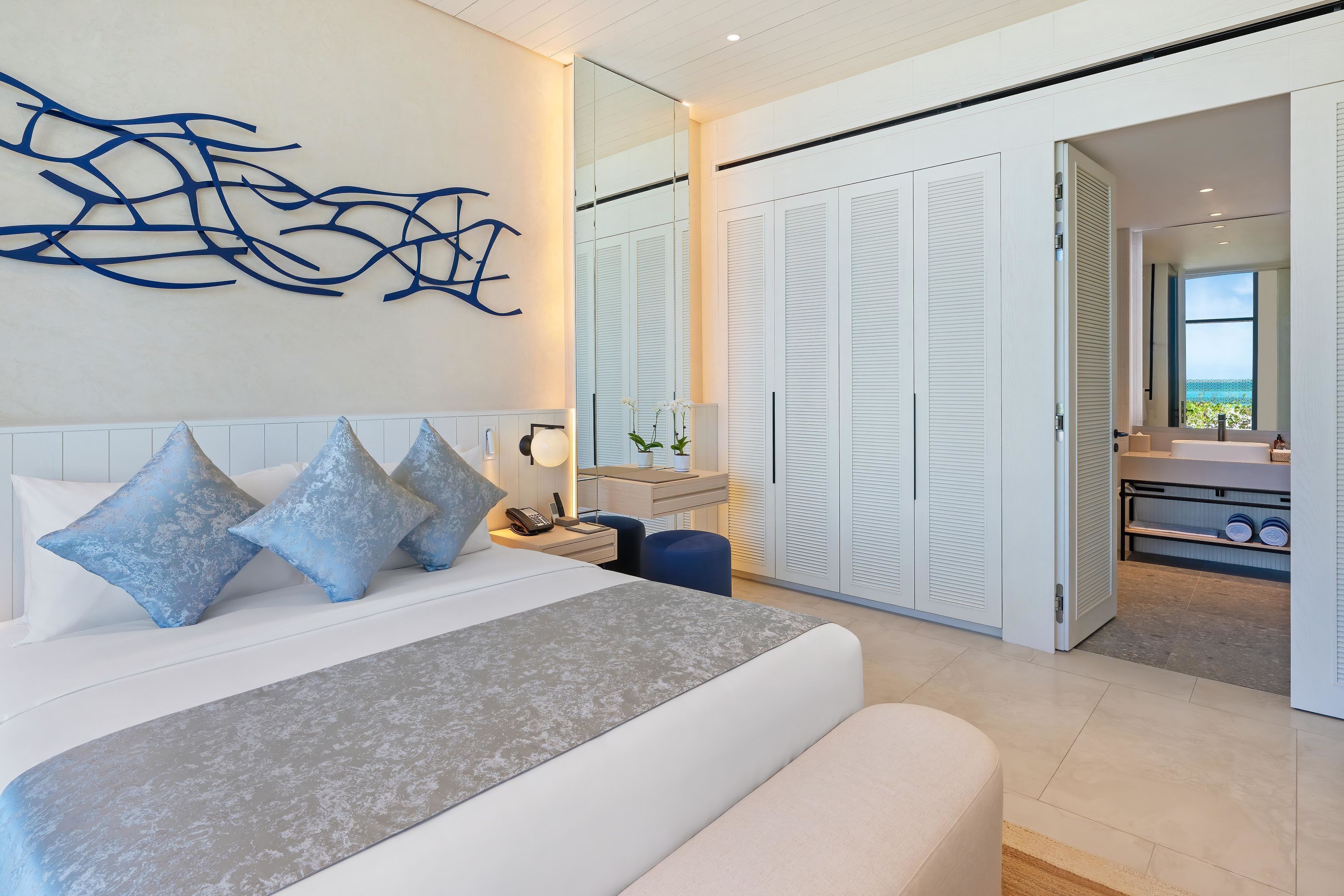 Une chambre à coucher moderne, dotée d’un grand lit, de tables de chevet, d’une commode et d’une salle de bain visible à travers une porte ouverte.