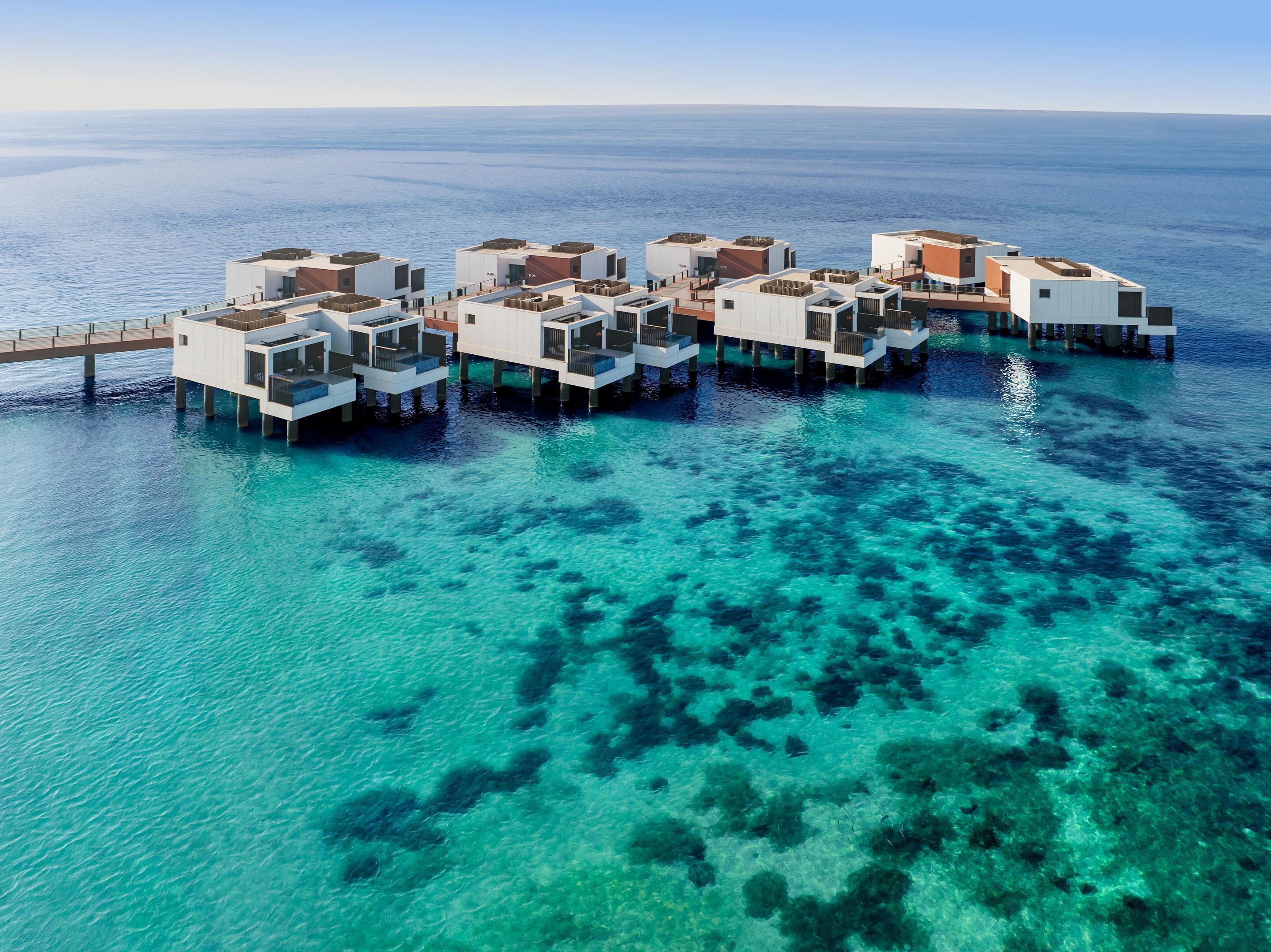 An overwater bungalow resort with multiple levels, clear blue waters, and a wooden walkway connecting the structures.