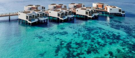 An overwater bungalow resort with multiple levels, clear blue waters, and a wooden walkway connecting the structures.