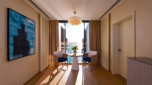 Habitación de hotel moderna con un ventanal grande, una mesa redonda con dos sillas, una planta en maceta y un cuadro en la pared.