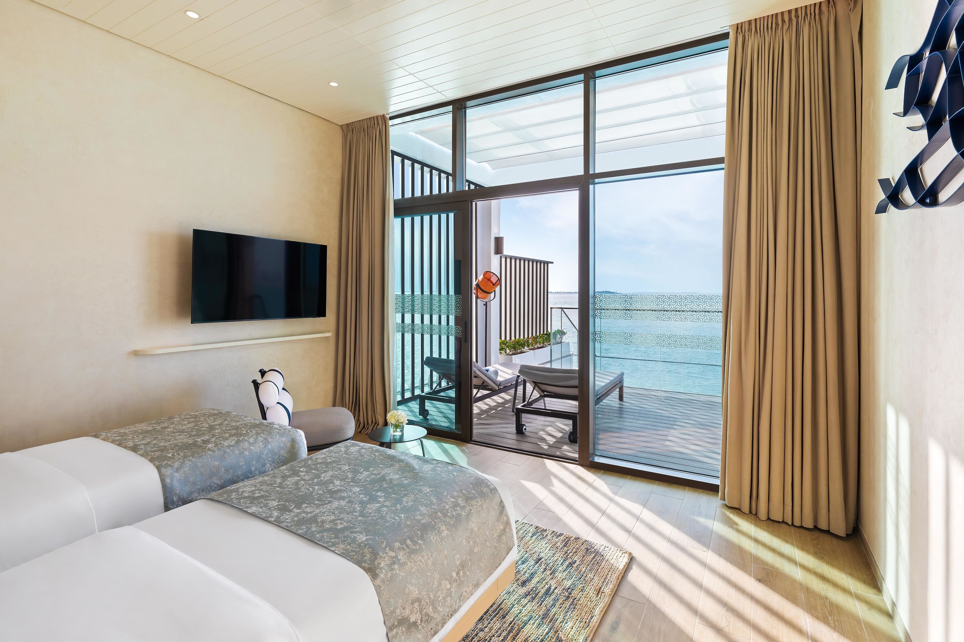 Una habitación de hotel moderna con una cama grande, un televisor montado en la pared y un balcón con vista al mar.