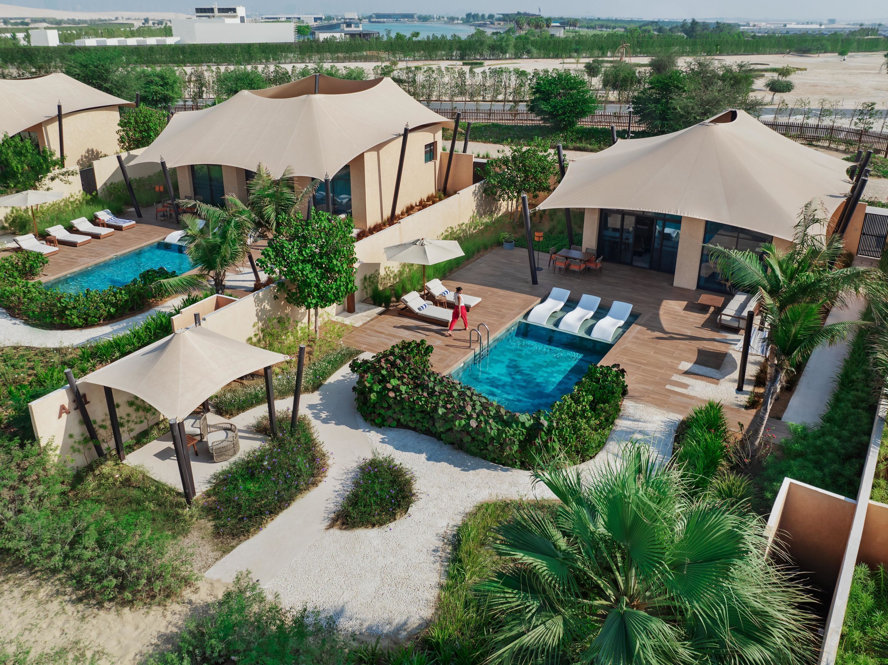 Un resort con múltiples piscinas, tumbonas y zonas a la sombra.