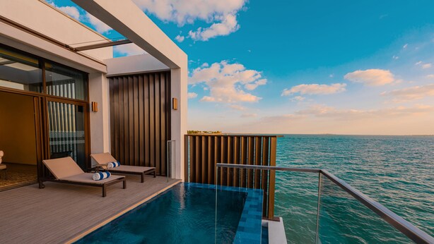 Zona de piscina exterior moderna con sillones de descanso y vistas al mar.