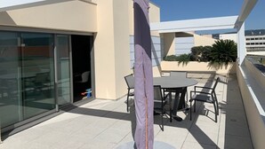 A rooftop terrace with a glass door entrance, outdoor seating, and a pergola structure. - Appartement à LA Ciotat Avec Grande Terrasse de 50m² à Deux pas du Vieux Port (LA CIOTAT)