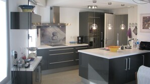 A modern kitchen with dark cabinetry, a central island, and pendant lighting. - Appartement à LA Ciotat Avec Grande Terrasse de 50m² à Deux pas du Vieux Port (LA CIOTAT)