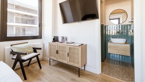A bedroom with a bed, a window, a TV, a cabinet, and a bathroom with a sink and mirror. - Cunabu Apartments Giolitti (Rome)