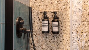 A bathroom with a shower, a hand dryer, and two bottles of shampoo. - Cunabu Apartments Giolitti (Rome)