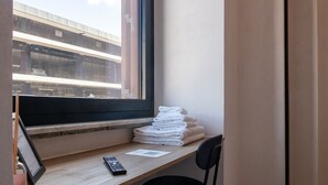 A hotel room with a desk, a chair, a window with a view of a building, and a stack of towels. - Cunabu Apartments Giolitti (Rome)