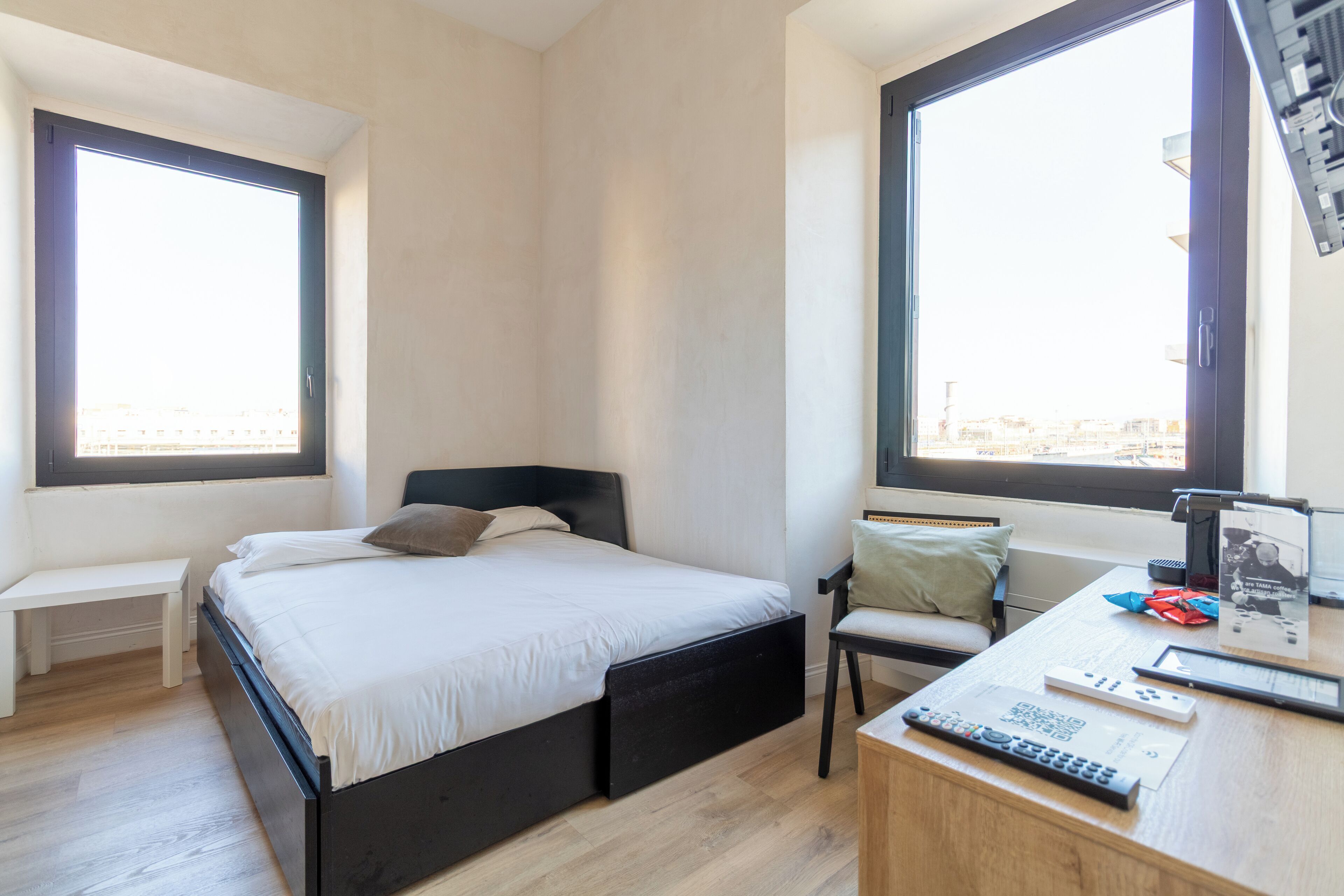 A bedroom with a bed, a desk with a chair, a bench, and two windows.