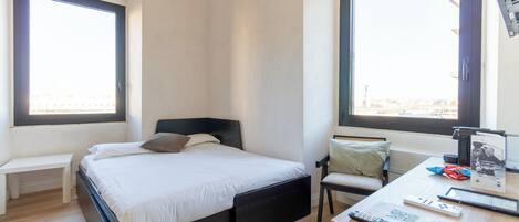 A bedroom with a bed, a desk with a chair, a bench, and two windows.