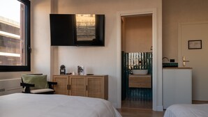 A bedroom with a bed, a chair, a TV mounted on the wall, a small cabinet, and a bathroom visible through an open door. - Cunabu Apartments Giolitti (Rome)
