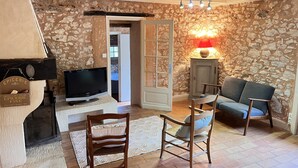 Un salon chaleureux avec des murs en pierre, une cheminée, un téléviseur et des fauteuils confortables.