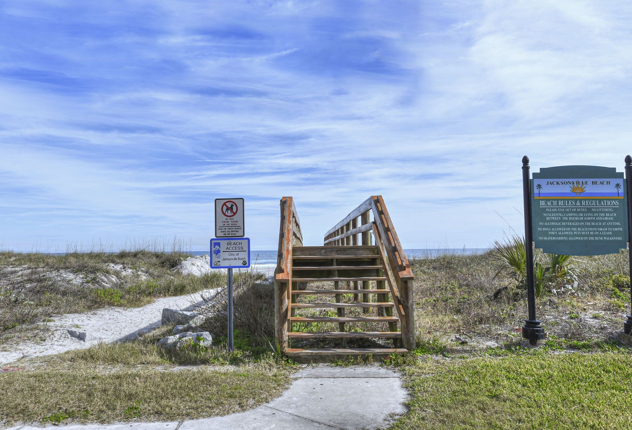 Eine Holztreppe führt zu einem Strand, wo ein Schild Strandregeln und -bestimmungen aufzeigt.