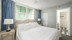 Ein ordentlich eingerichtetes Schlafzimmer mit einem Bett, Nachttischen, einem Deckenventilator und Blick ins Badezimmer.