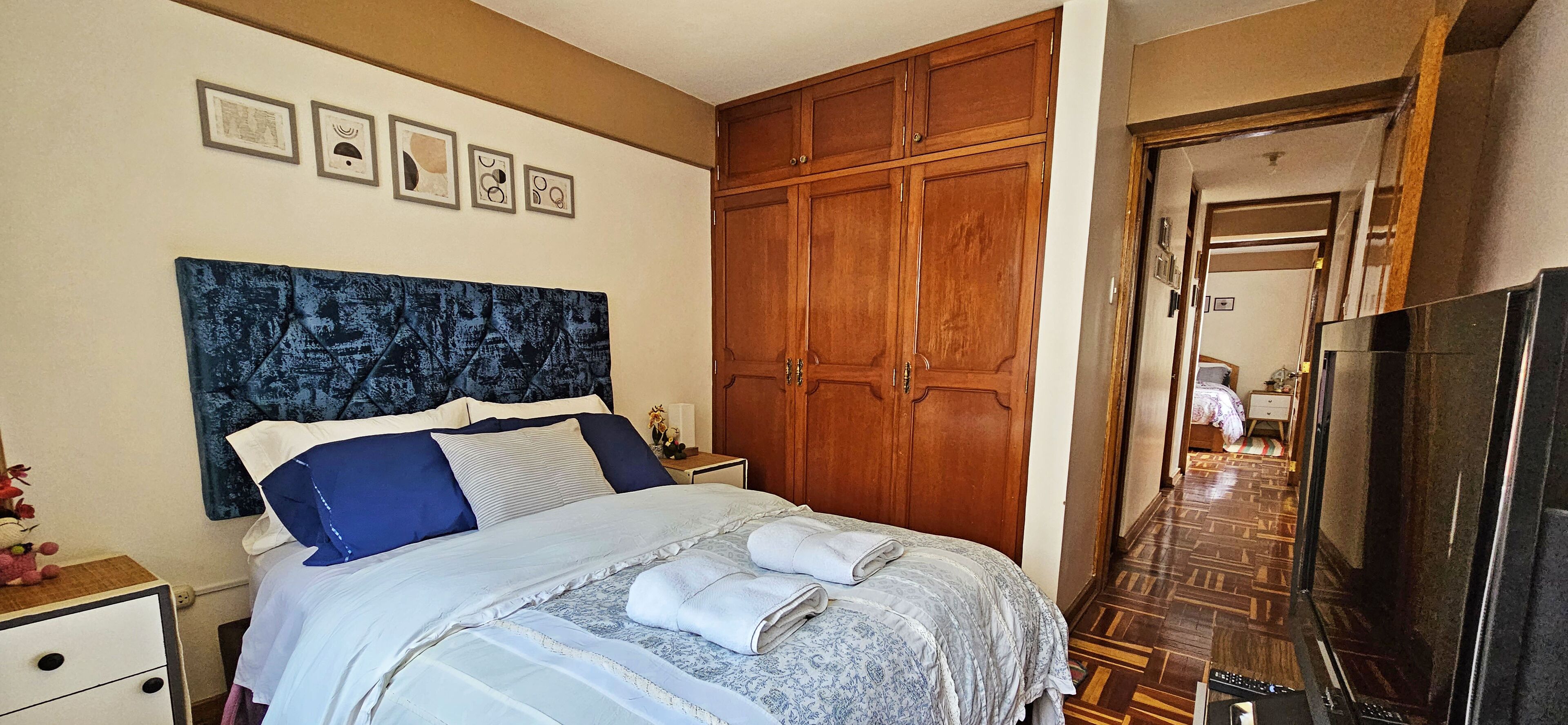 A bedroom with a large bed, wooden wardrobe, and a television.