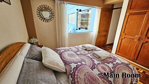 Una stanza principale con un letto, una finestra con vista, un armadio in legno e uno specchio decorativo appeso al muro.