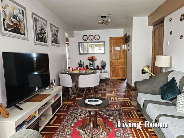 A living room with a flat-screen TV, a sofa, a coffee table, and a dining area with chairs and a table. - Pama Wasi - Casa del Puma (Cusco)
