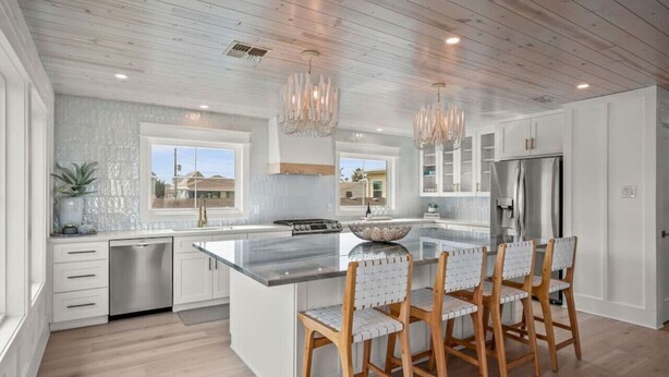 A modern kitchen with a large island, stainless steel appliances, and wooden chairs. - Upscale Custom Home w Golf Cart / Outdoor Bar / Mins to Beach! (Port Aransas)
