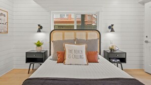 A bedroom with a bed, two bedside tables, a window, and a view of a building outside. - Upscale Custom Home w Golf Cart / Outdoor Bar / Mins to Beach! (Port Aransas)