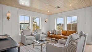 A spacious living room with a wooden ceiling, large windows, and a mix of seating options including a sofa and chairs. - Upscale Custom Home w Golf Cart / Outdoor Bar / Mins to Beach! (Port Aransas)