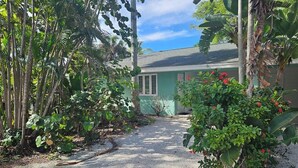 A house with a gravel driveway, surrounded by lush tropical vegetation.
