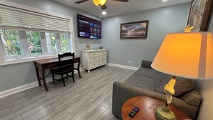 A living room with a ceiling fan, a TV mounted on the wall, a dining area with a table and chairs, and a sofa.