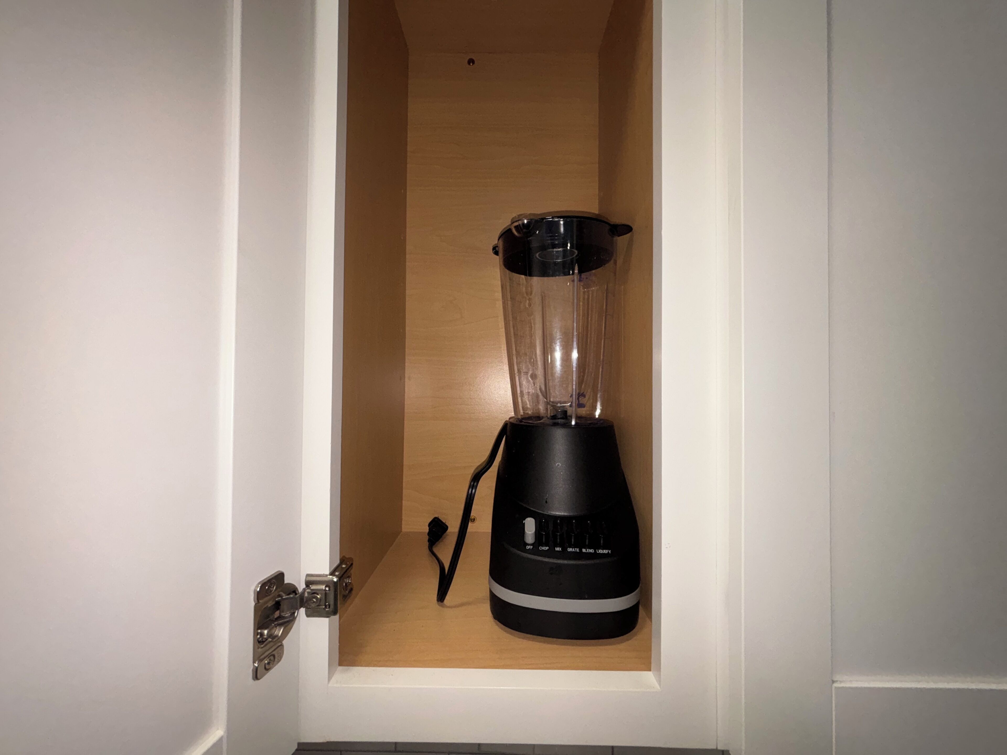 Un mixeur noir, placé dans un meuble blanc dont l’intérieur est en bois.