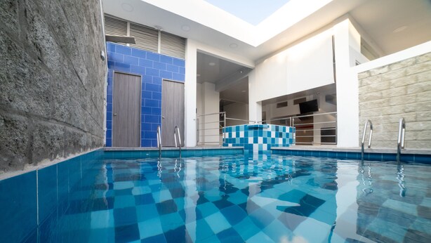 A modern indoor swimming pool with a checkered tile pattern, surrounded by stone walls and a blue-tiled wall. - HOTEL SANTA MARTA TROPICAL (Santa Marta)