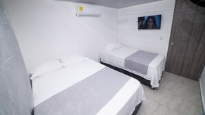 A hotel room with two beds, a TV on the wall, and a door. - HOTEL SANTA MARTA TROPICAL (Santa Marta)