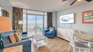 Ein Wohnzimmer mit einer Couch, einem Sessel, einem Couchtisch und einem Fernseher, der 'Ocean Wave Rentals' anzeigt.