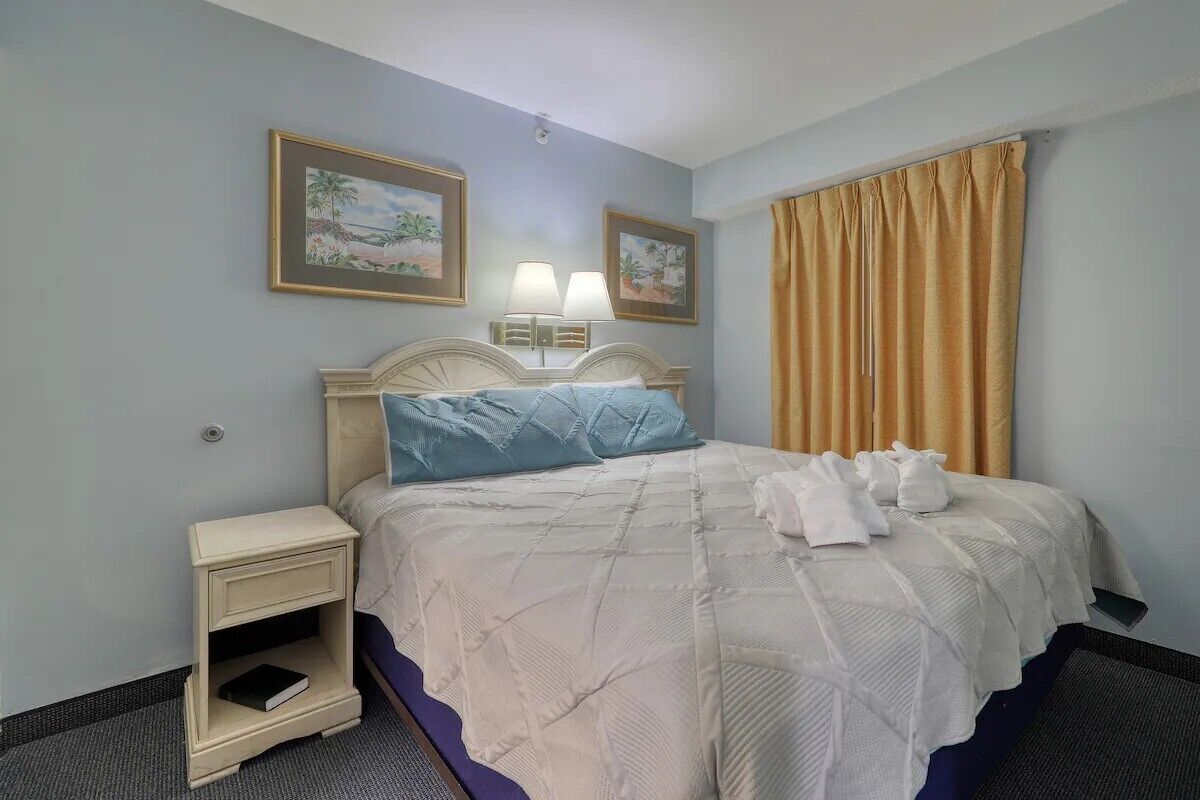 A hotel room with a bed, bedside tables, a lamp, and two framed pictures on the wall.