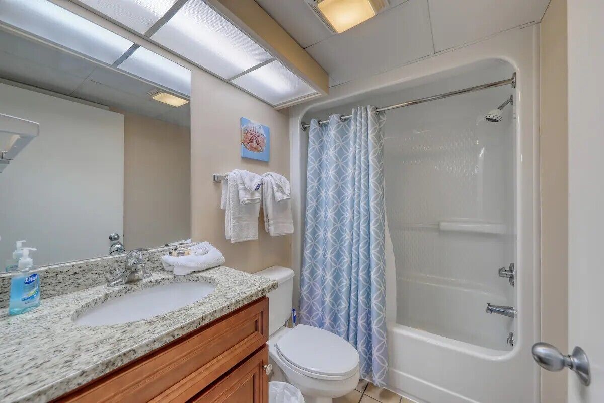 A bathroom with a granite countertop sink, a toilet, a shower with a glass door, and a towel rack with towels.