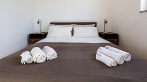 Una cama bien hecha con sábanas blancas y dos toallas enrolladas encima.