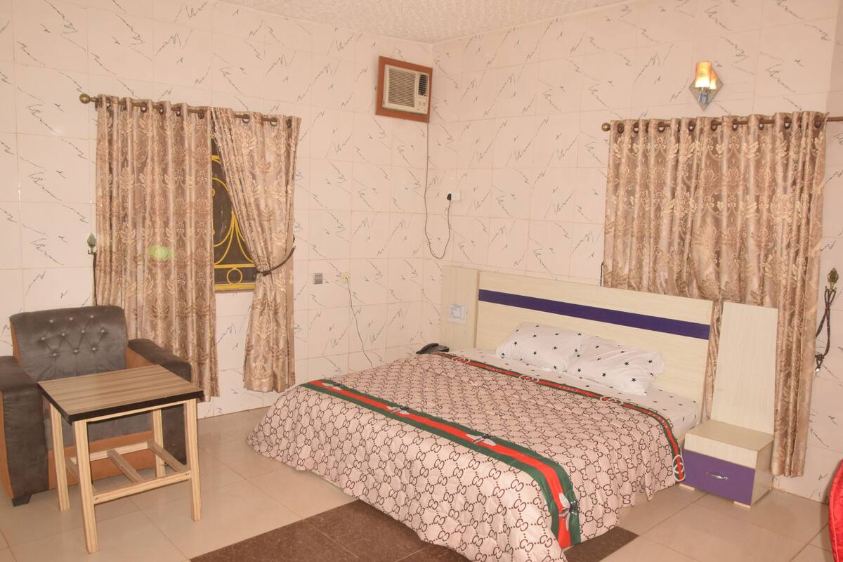 A bedroom with a bed, a chair, a table, and curtains.