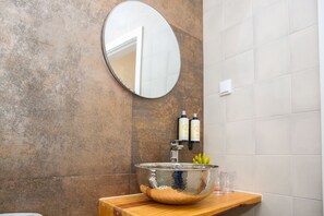 A bathroom with a round mirror, a large metallic bowl sink, and two bottles of toiletries on a wooden shelf. - Pata da Gaivota Boutique House (Lourinha)