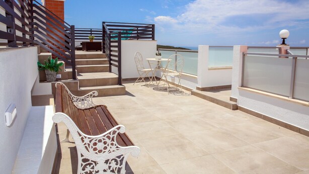 A rooftop terrace with a wooden bench, a table, and chairs, a staircase, and a view of the sea. - Pata da Gaivota Boutique House (Lourinha)