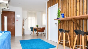 A modern living room with a blue rug, wooden furniture, and a dining area with chairs and a table. - Pata da Gaivota Boutique House (Lourinha)